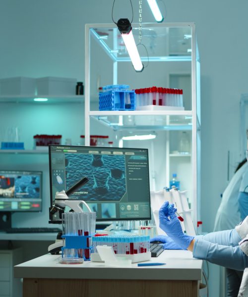 Medical lab worker analyzing blood serum conducting virus test in modern equipped lab late at night. Team of specialists examining vaccine evolution using high tech for treatment against covid19